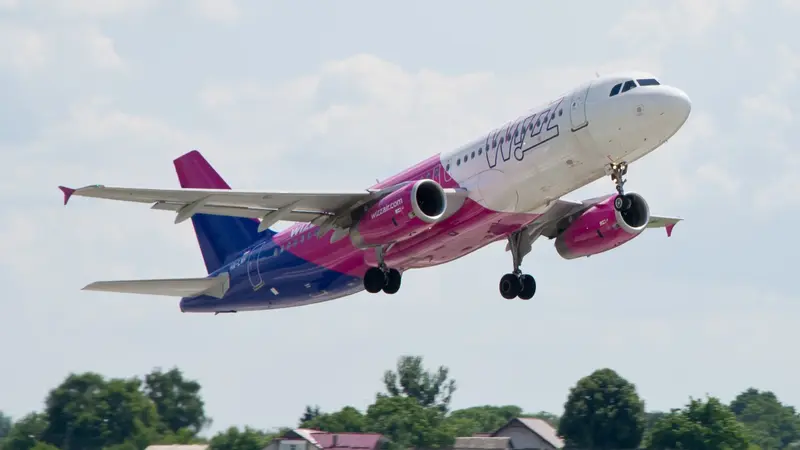 Letadlo Wizz Air s růžovo-fialovým trupem při vzletu, podvozek ještě venku